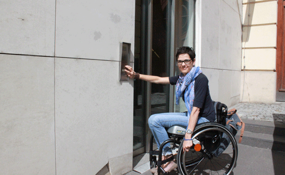 Maria Sobotka klingelt am Eingang für Rollstuhlfahrer vor dem VERBUND-Gebäude