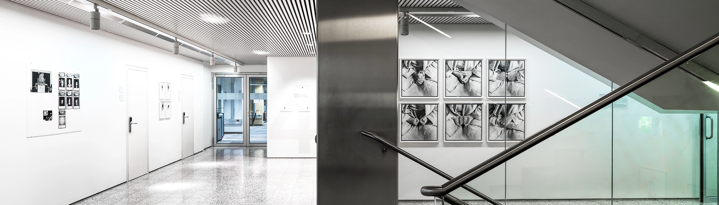 Wir blicken in die Vertikale Galerie in Wien. Wir sehen ein Stiegenhaus in hellen Tönen gehalten. An den Wänden sind Fotographien ausgestellt.