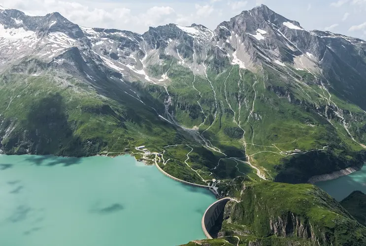 dam wall. Behind them, high mountains in summer. The light blue sky is illuminated by the sun.