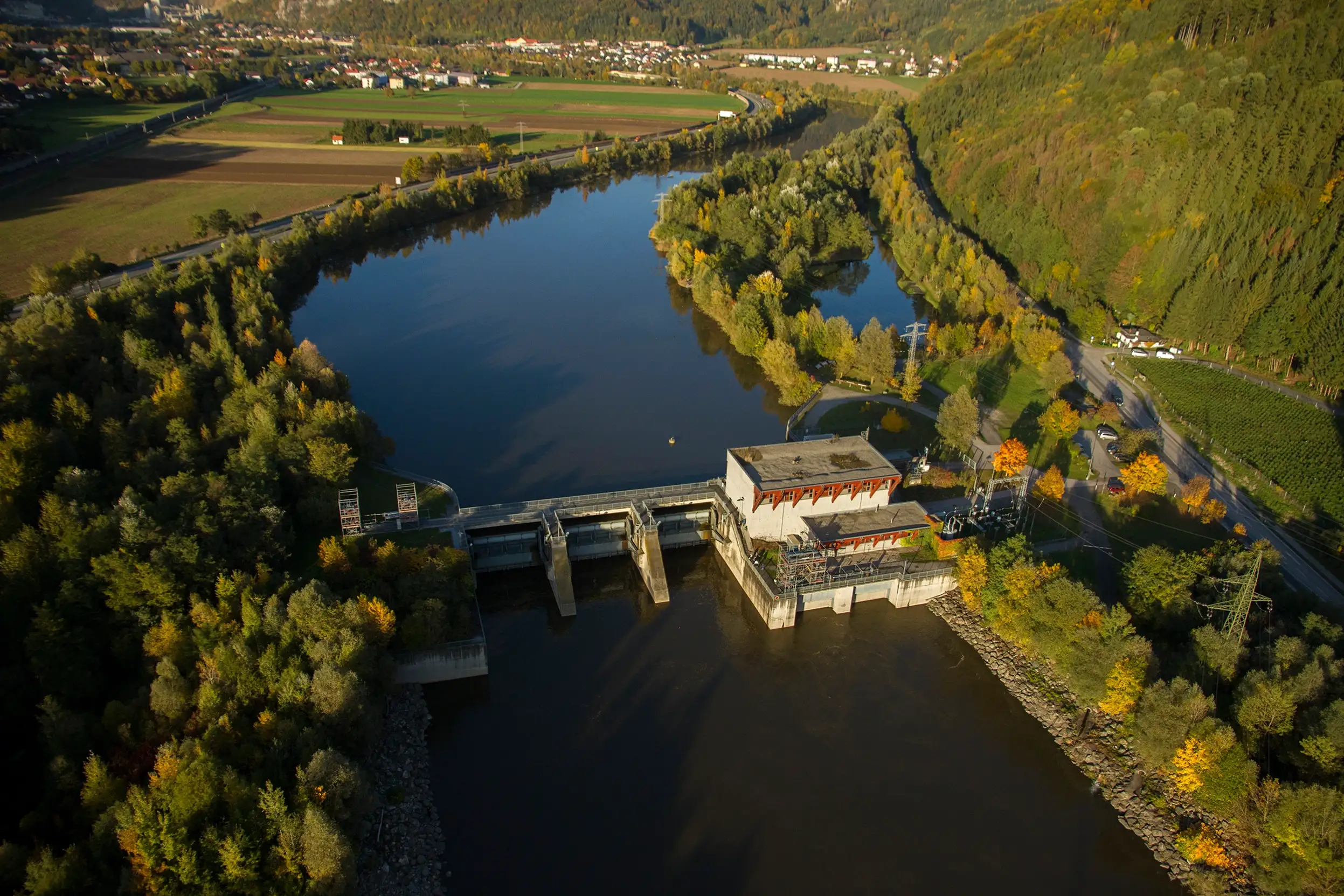 We look down on the Friesach and Mur run-of-river power station from above. The sun is low. The mood is autumnal.