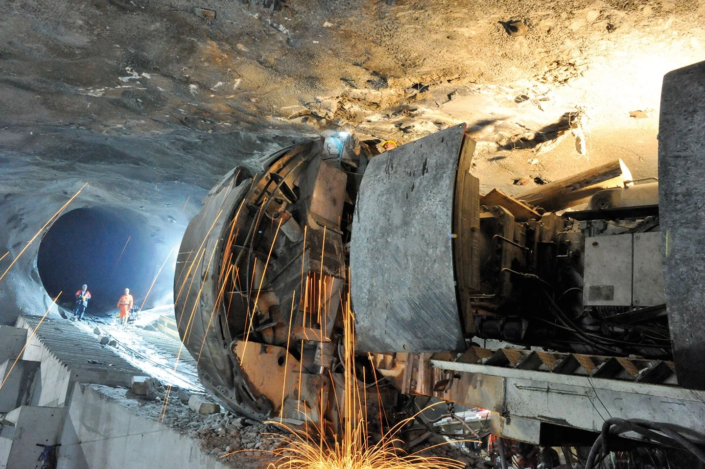 You can see a tunnel of the Limberg power station into which the drill head is being brought. The spotlights illuminate the dark shaft and two employees in protective clothing are just coming out of the tunnel