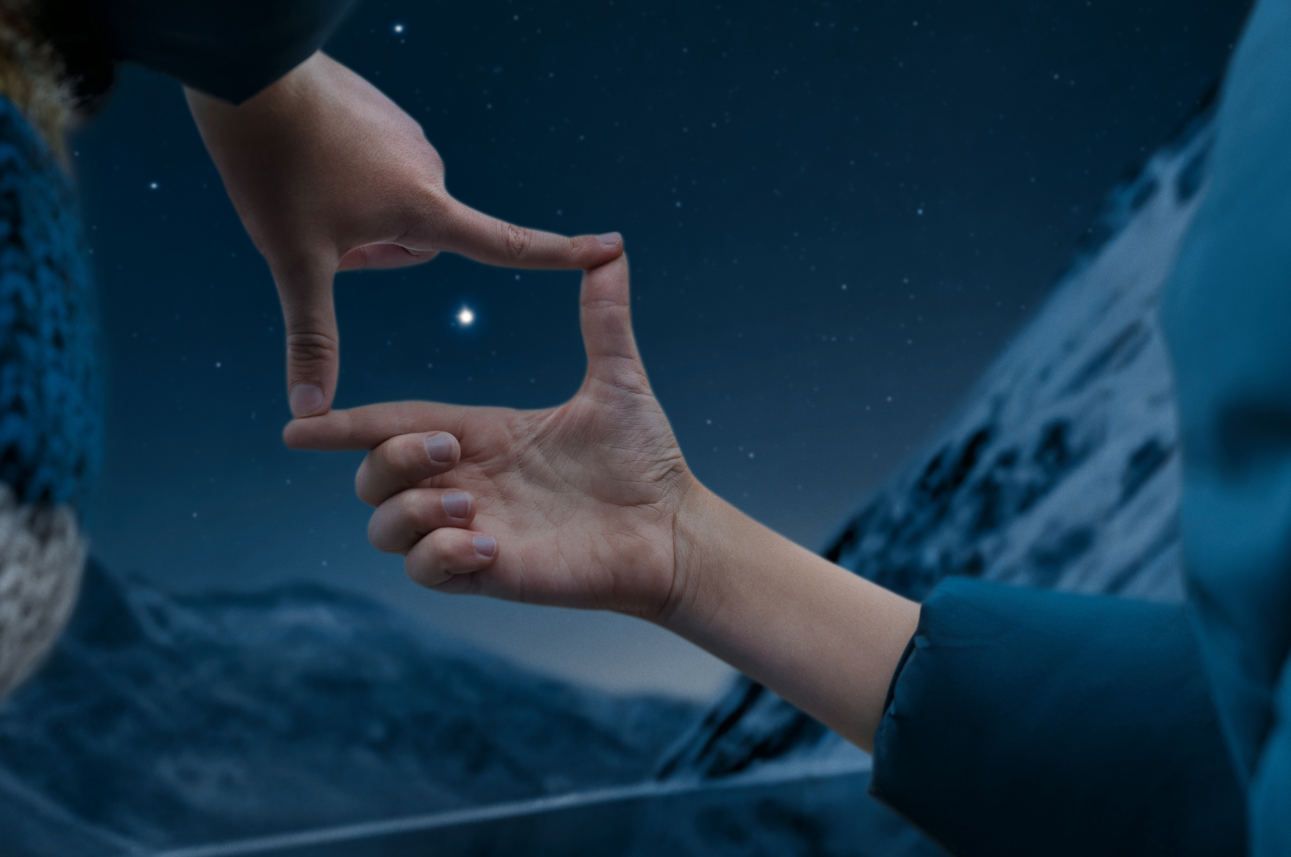Wir sehen zwei Kinderhände. Sie formen ein Rechteckt. Im Mittelpunkt des Rechtecks sehen wir einen stark leuchtenden Stern am Nachhimmel.