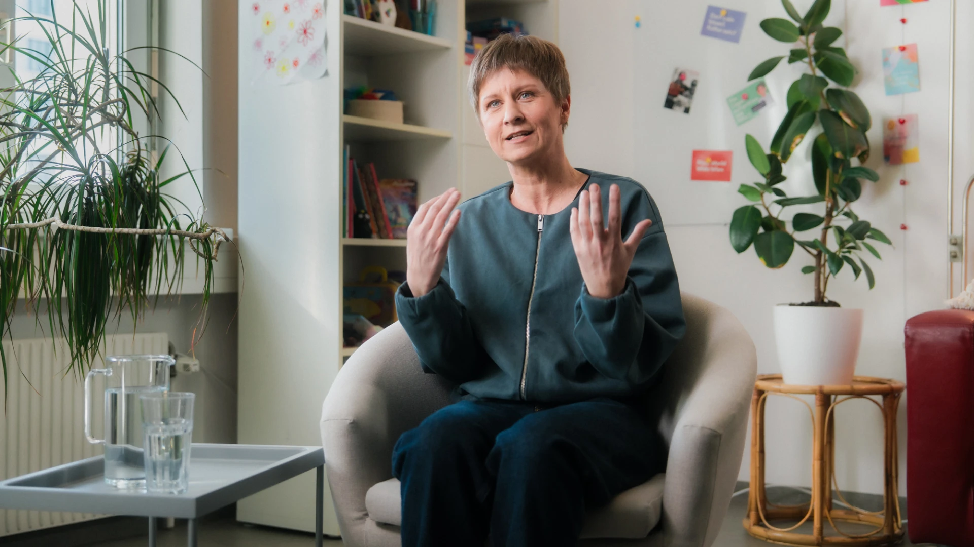 Eine Frau mit kurzen blonden Haaren und blauen Augen ist gerade dabei etwas einen Zuhörer zu erklären.