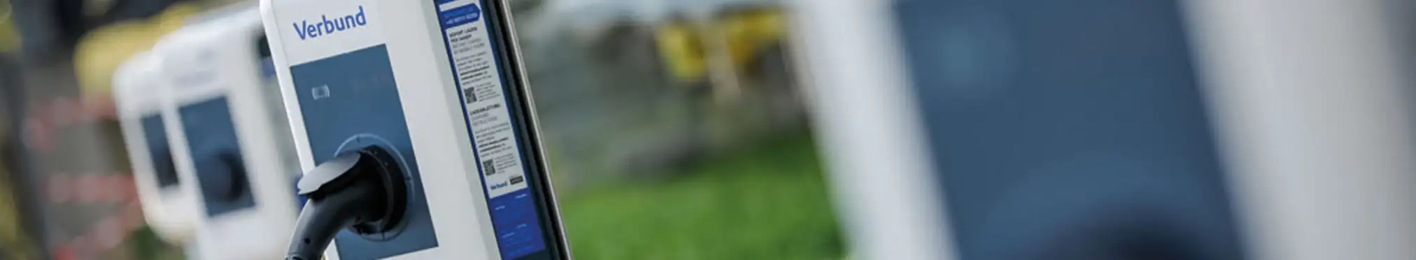Mehrere VERBUND Ladestationen an einem Firmenstandort, im Hintergrund ist eine grüne Wiese zu sehen.