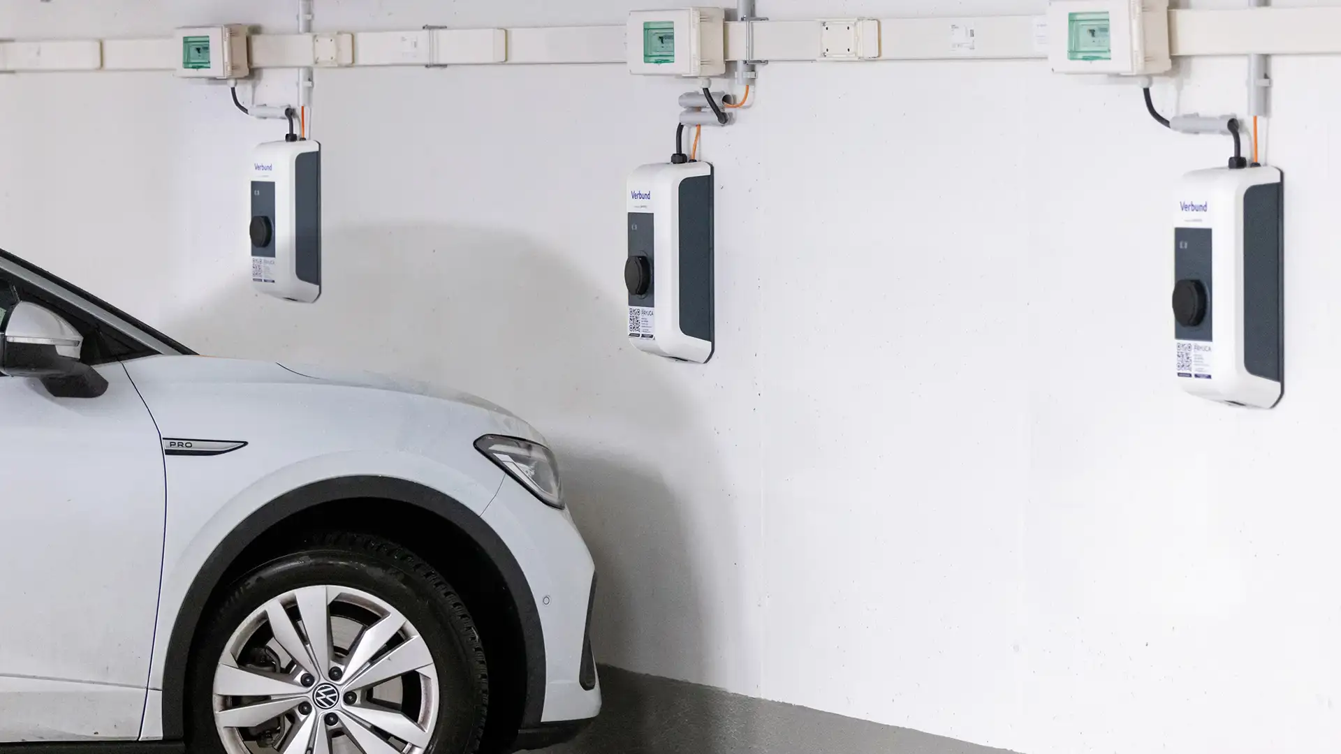 An electric vehicle is charging at a VERBUND charging station in a parking garage.