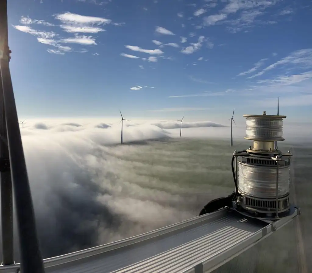 Wir blicken auf eine Windfarm in Spanien. Wir sehen Windräder und Wolken.