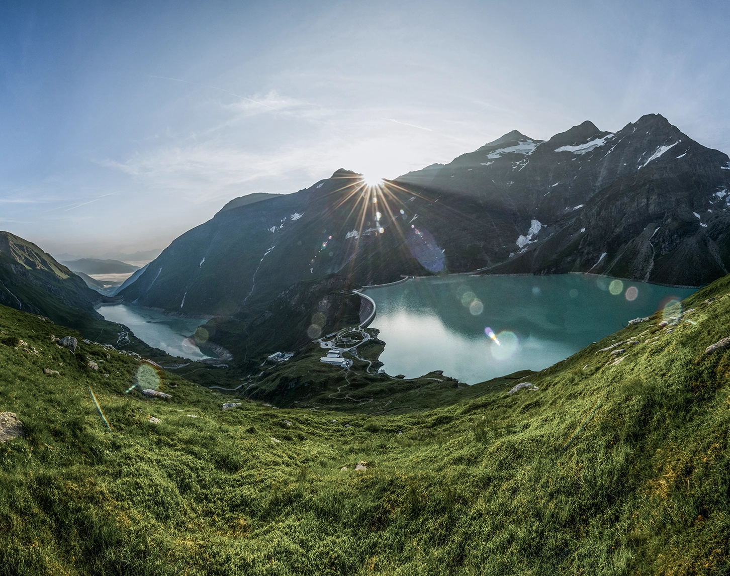 We look out over the Kaprun reservoirs at sunrise. The sun peaks over the Alps, creating an interesting lighting mood.