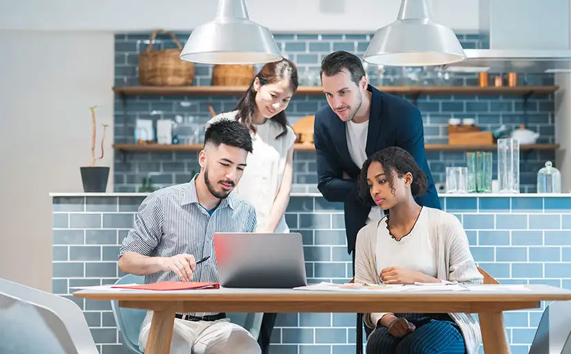 Vier junge Menschen sind versammelt in einem Gemeinschaftsraum und blicken auf einen Laptop.
