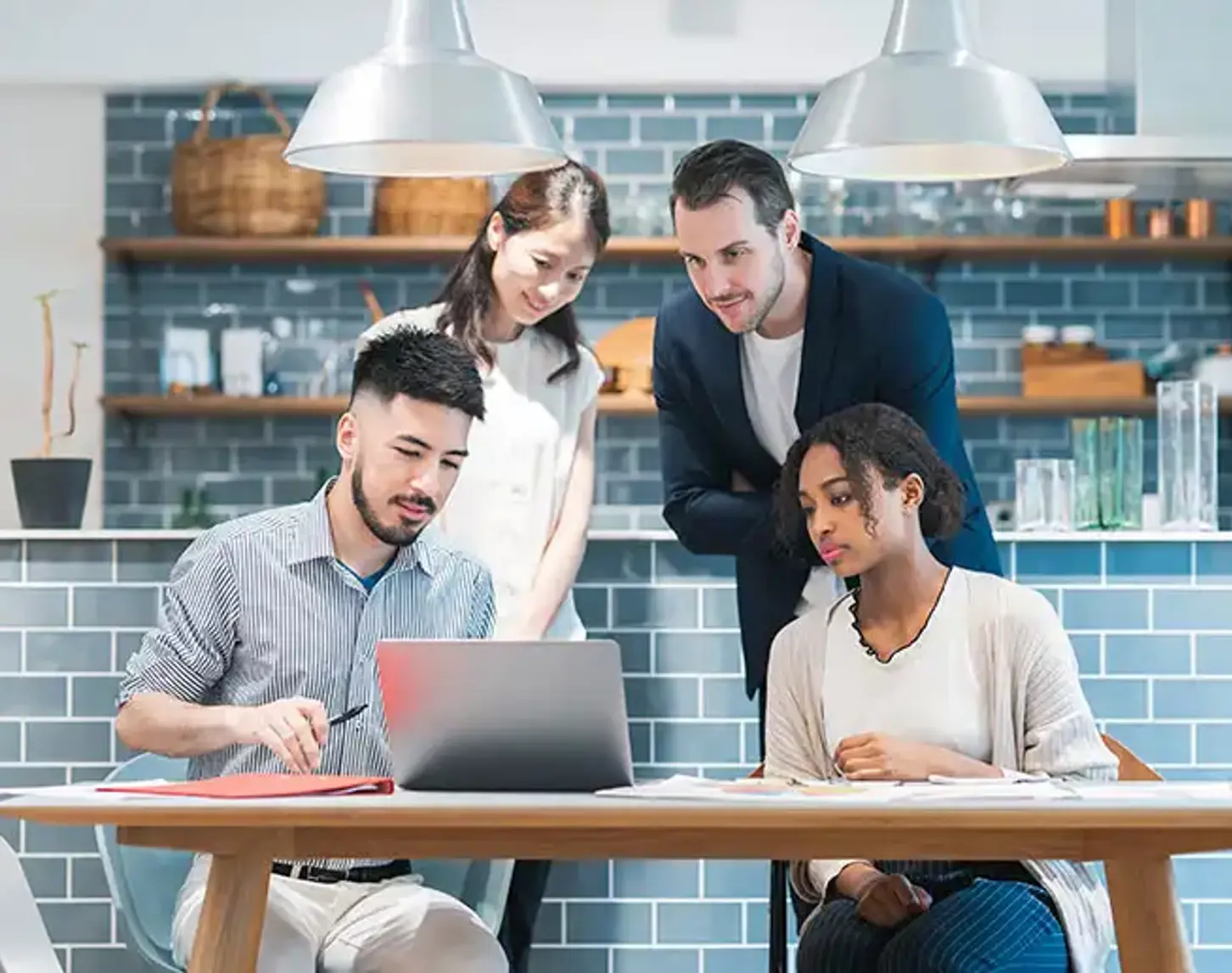 Four young people are gathered in a common room, looking at a laptop.