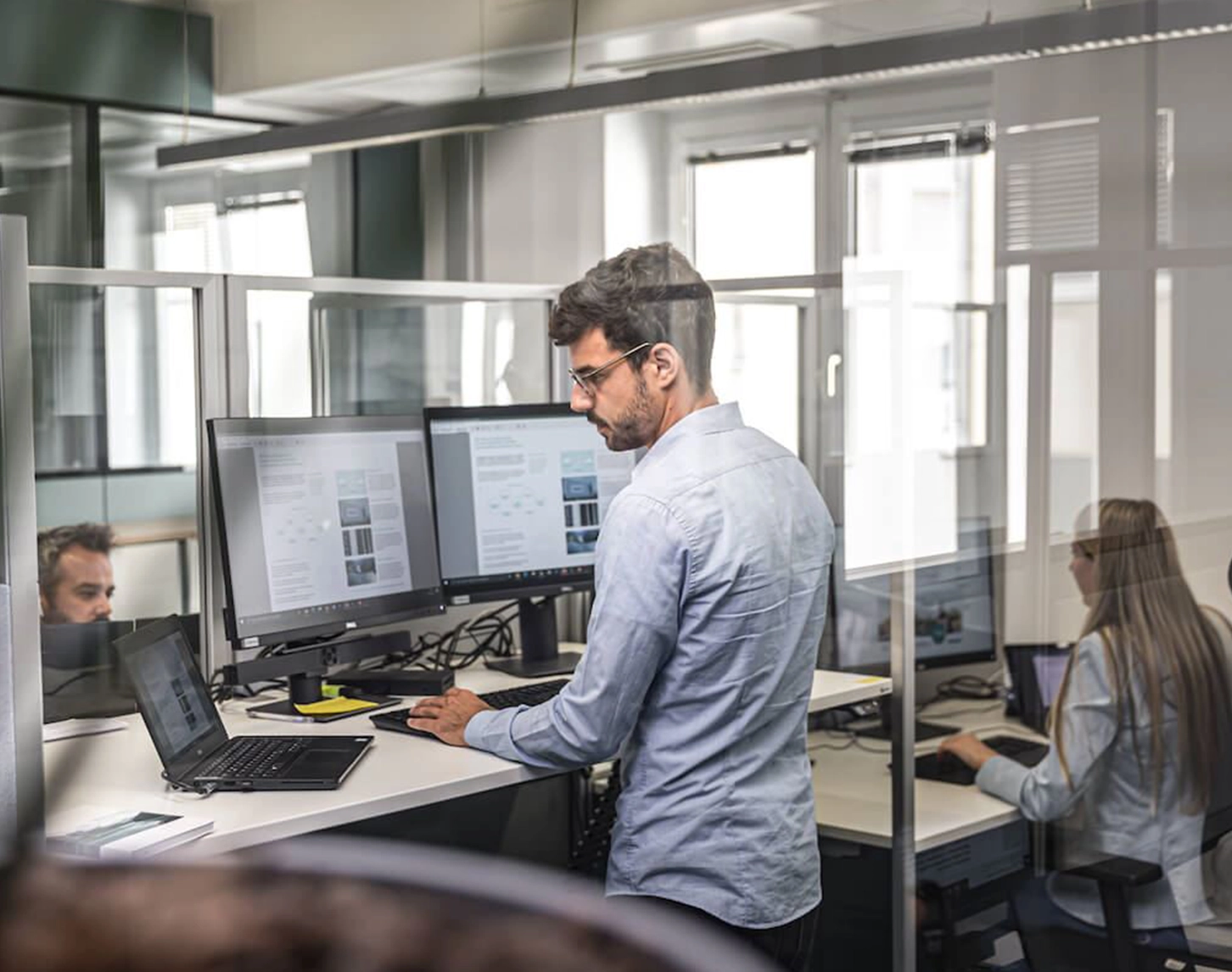 We look into an open-plan office. Three VERBUND employees are absorbed in their work. The large windows let in plenty of daylight.