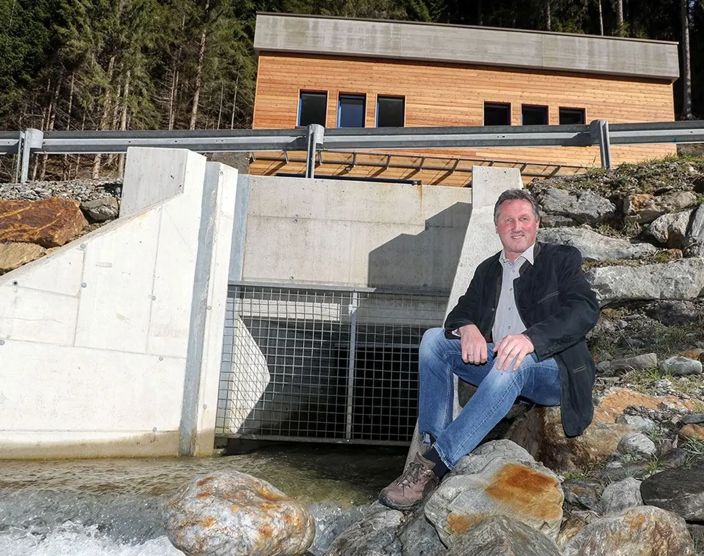 Dieses Bild zeigt eine Person, die auf einem Felsen neben einem Wasserkraftwerk sitzt.