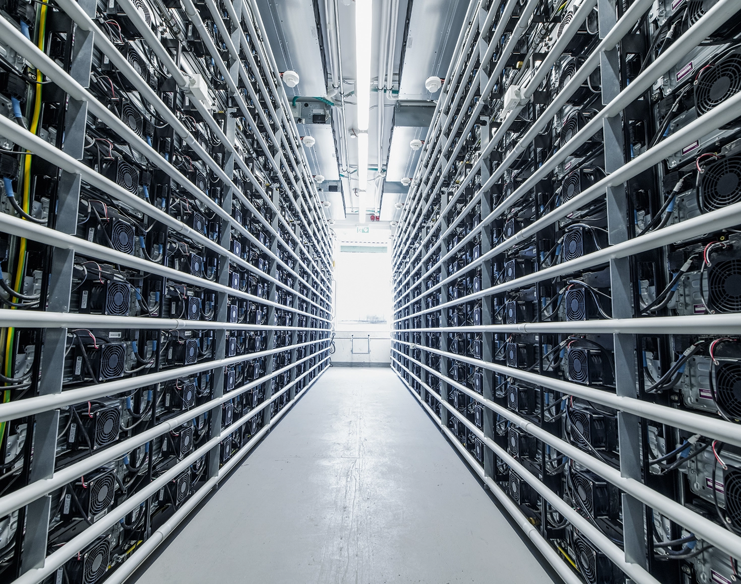 A look inside a battery storage system. A bright corridor is lined with numerous batteries to the right and left.