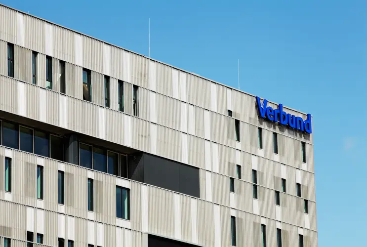 Wir blicken auf die Fassade von VERBUND am Westbahnhof. Diese ist grau mit Fenstern. Oben rechts steht in VERBUND-blau der VERSBUND-Schriftzug.