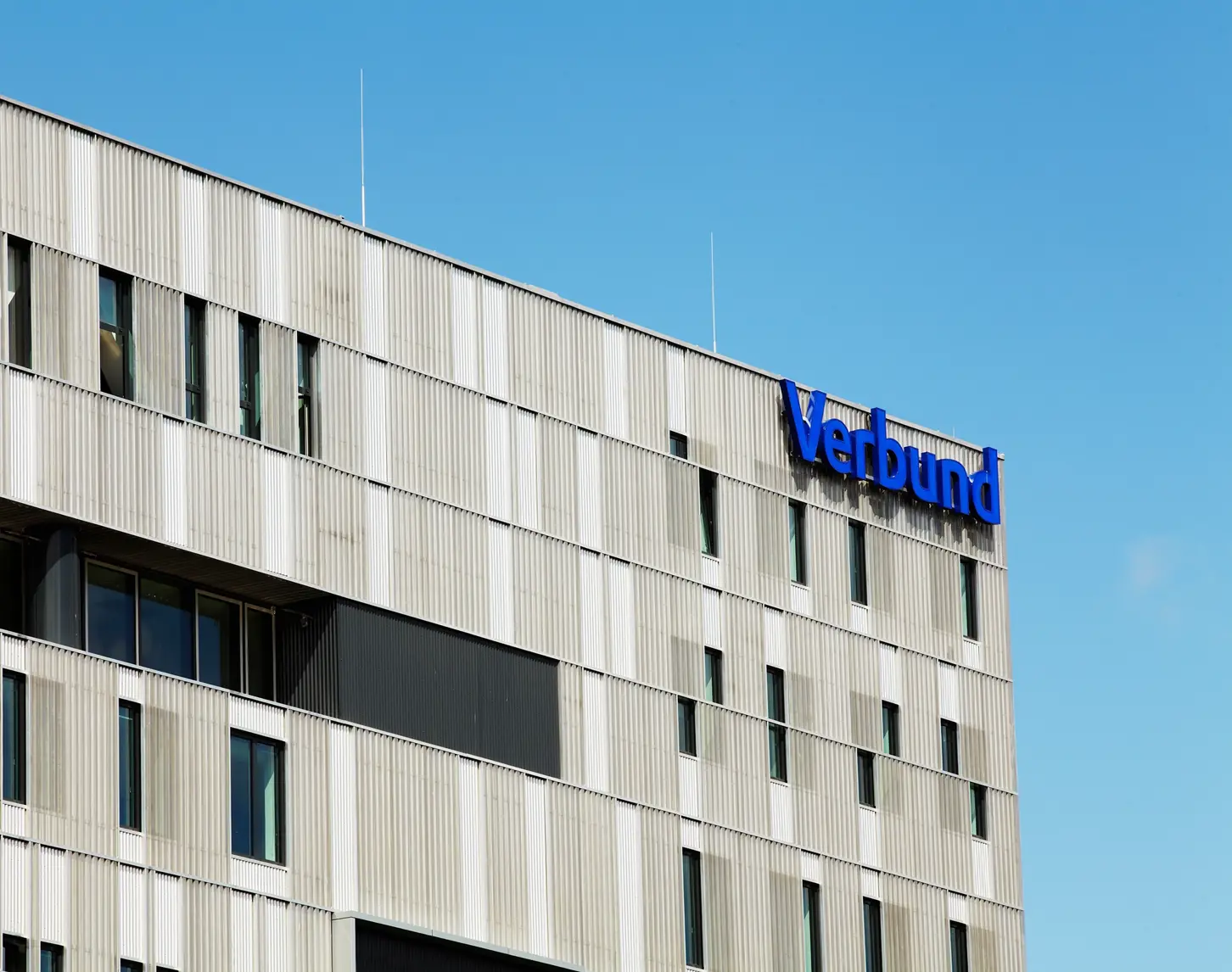 Wir blicken auf die Fassade von VERBUND am Westbahnhof. Diese ist grau mit Fenstern. Oben rechts steht in VERBUND-blau der VERSBUND-Schriftzug.