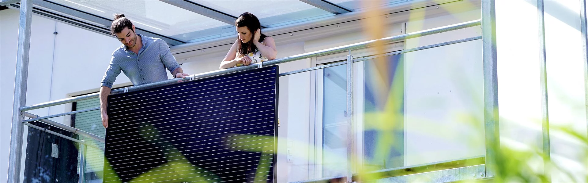 Wir blicken auf ein Pärchen, das ein Solarpanel am Balkon befestigt.