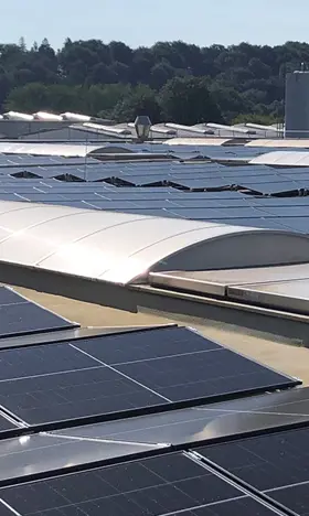 Eine große PV-Anlage auf einem Dach einer Industrieanlage, in den Paneelen spiegelt sich das Sonnenlicht.