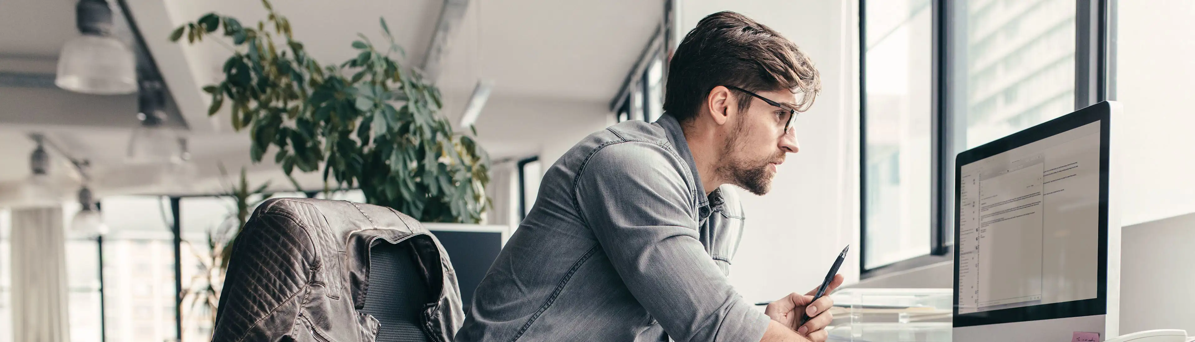 Ein Mann sitzt in einem Büro und arbeitet mit konzentriertem Blick an seinem Laptop.