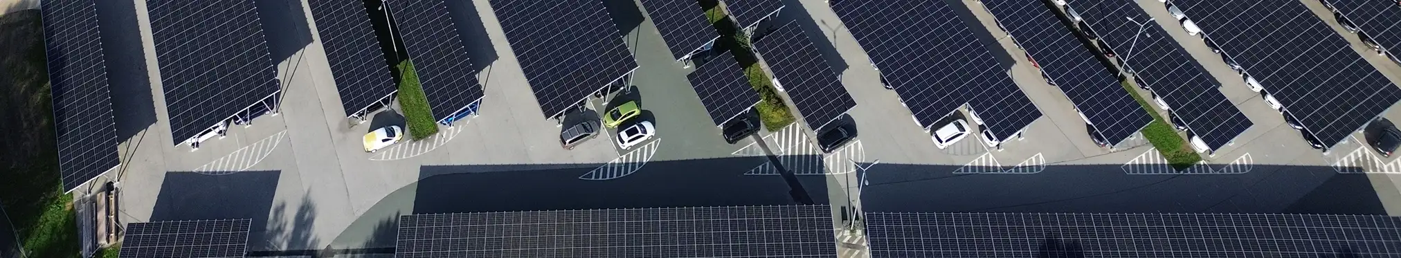 Vogelperspektive auf eine große Carport-Photovoltaik Anlage mit darunter geparkten Elektroautos.