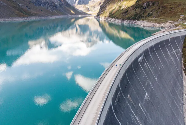The white clouds are reflected in a marvellously blue reservoir. The dam wall can be seen on the right-hand edge of the picture. The Alps peak out in the background.