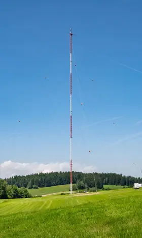 The picture shows the Wendmess mast, which collects ecological information on the Schiffberg. The weather is wonderfully sunny and the meadows are green.