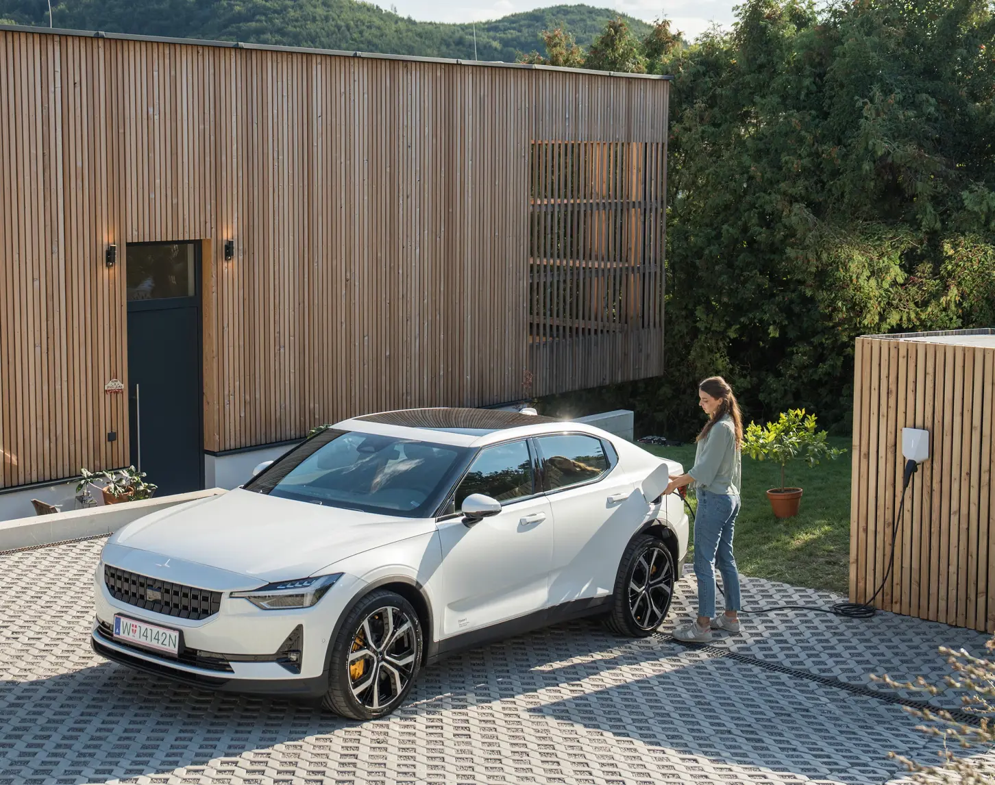 Eine Frau die ihr weißes Elektroauto an eine Wallbox anschließt.