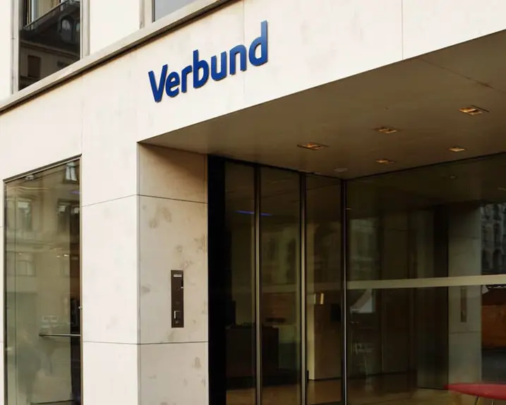 You can see the entrance area of the VERBUND headquarters at Am Hof 6A. The building has a beige front with high windows, on the right is the entrance area with a glass front and the VERBUND logo above it.