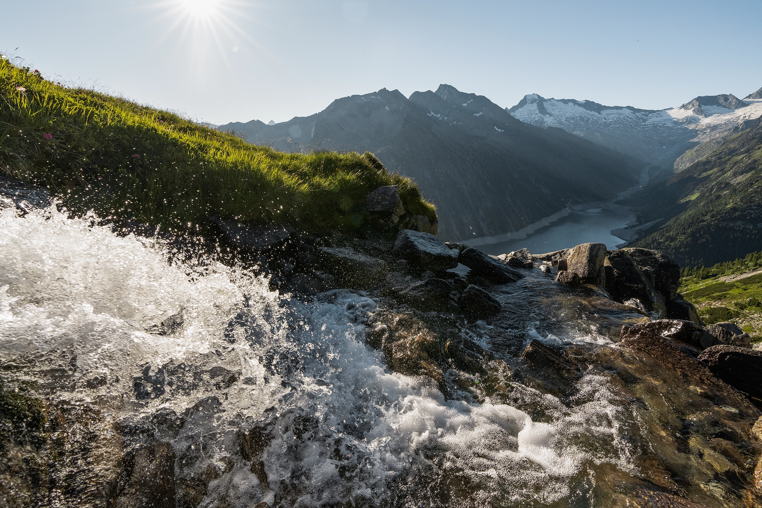 Ein Bergbach bahnt sich seinen Weg in die Tiefe. Die Sonne strahl und der Himmel ist blau.