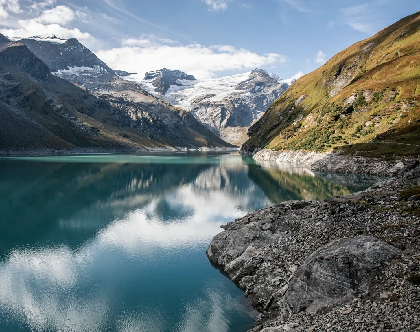 Wir blicken auf einen See, der von Bergen und Hügeln umgeben ist.