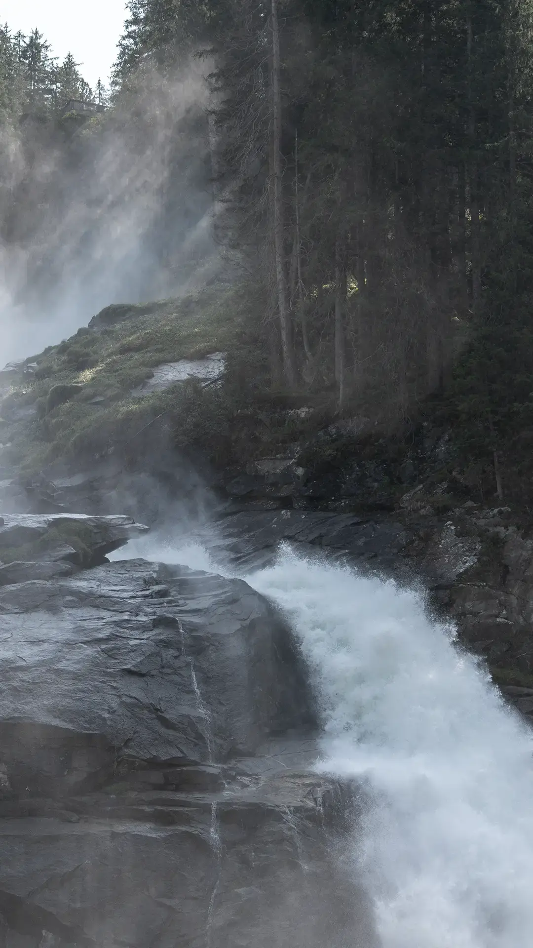 Wir blicken auf einen Wasserfall, Gestein und einem mystisch anmutenden Wald.