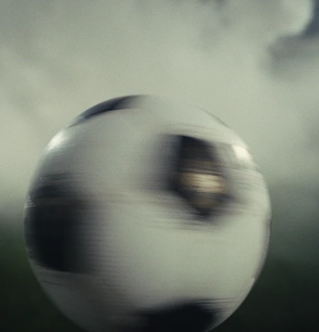 Eine Person in violetter Fußballkleidung spielt einen Fußball vor dunklem, rauchigem Hintergrund; die Zahl 14 ist auf der Hose zu sehen.
