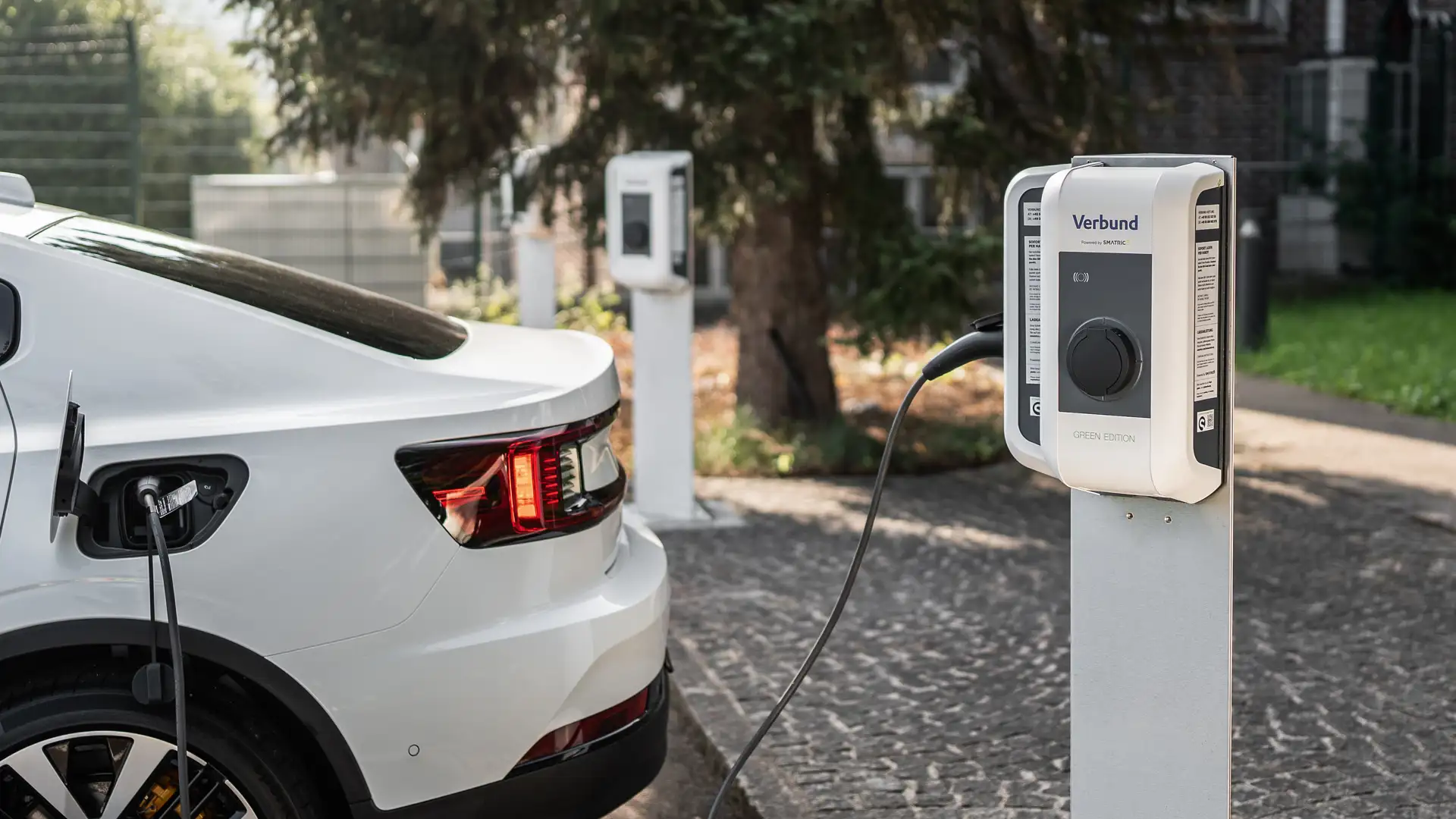 An electric vehicle is charging at a VERBUND charging station in the parking lot of a company location.